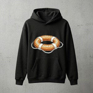 May include: Black hooded sweatshirt featuring a graphic of a life preserver. The life preserver is orange with white stripes and a rope detail. The sweatshirt has a front pocket and a drawstring hood.