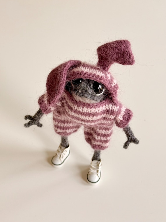 A hand-needle-felted frog dressed in a tiny bunny outfit with a ghostly vibe — the kind of unsettling-yet-adorable creature you didn't know you needed on your shelf.