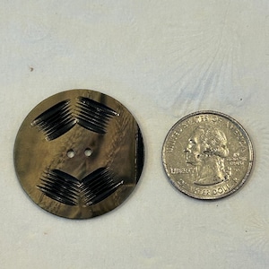 May include: A large, round, antique button with a dark, mottled finish and two holes. The button has a series of etched, chevron-like patterns. A US quarter is next to the button for size comparison.