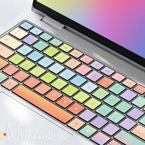 Peut inclure: Un ordinateur portable argenté doté d'un clavier avec une protection aux tons pastel dégradés orange, jaune, vert, bleu et violet. L'écran affiche un fond arc-en-ciel vibrant avec le texte cursif blanc Customizable et le logo Art Nathaniel.