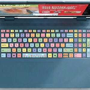 May include: A dark blue laptop featuring a custom keyboard skin with multi-colored keys in shades of pink, yellow, blue, and purple. The space bar displays a floral pattern, and the screen shows a red and green graphic with the text better eats.