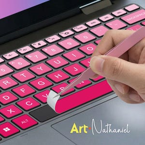 May include: A laptop keyboard with pink key stickers being applied with pink tweezers. The keyboard keys are a gradient of pink shades. The text "Art Nathaniel" is in the bottom right corner.
