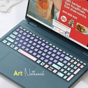 K&ouml;nnte beinhalten: Ein dunkelblauer Laptop mit einer individuellen Tastaturfolie in Hellblau, Lavendel und Rosa. Der Bildschirm zeigt eine rote Webseite mit dem Text Get better eats. Get healthier. Get discounts. Auf dem Touchpad steht der Text Art Nathaniel.