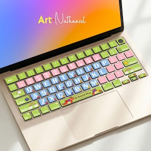 Könnte beinhalten: Ein Laptop mit einer farbenfrohen Tastaturabdeckung. Die Abdeckung hat grüne, rosa und blaue Tasten mit weißen Buchstaben und Cartoon-Illustrationen. Der Bildschirm zeigt den Text "Art Nathaniel" in Gelb. Der Satz "A Happy Day" ist ebenfalls sichtbar.