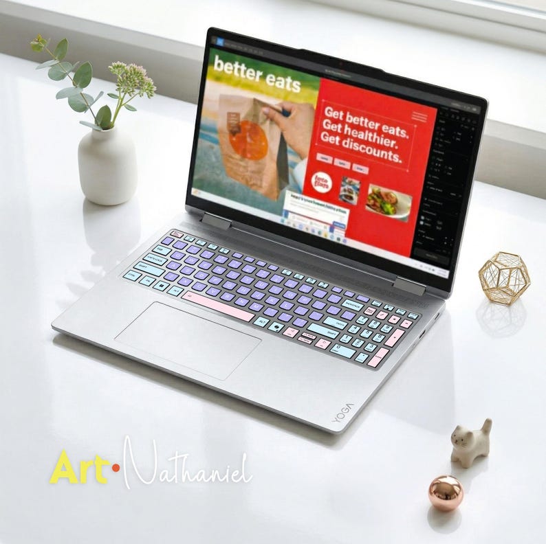 K&ouml;nnte beinhalten: Ein silberner Laptop mit einer individuellen Tastaturabdeckung mit hellblauen und violetten Tasten. Der Bildschirm zeigt eine Website mit dem Text better eats, Get better eats. Get healthier. Get discounts. Das Yoga-Logo ist auf der Handballenauflage.