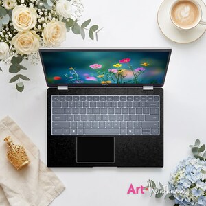 Op de afbeelding: Een Dell-laptop met een zwarte, getextureerde skin op het toetsenbord en de polssteun. Het scherm toont een levendige bloemenweide met roze, gele en rode bloemen. De laptop is omringd door witte rozen, een kopje koffie en een gouden flesje.
