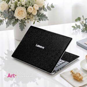 Op de afbeelding: Een zwarte Lenovo-laptop met een getextureerd, gemarmerd patroon op de buitenkant van het deksel. De laptop staat open en toont een zwart toetsenbord en zilverkleurige poorten aan de zijkant. De merknaam Lenovo staat in witte letters.