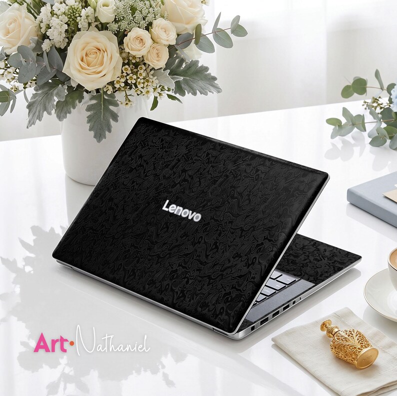 Op de afbeelding: Een zwarte Lenovo-laptop met een getextureerd, gemarmerd patroon op de buitenkant van het deksel. De laptop staat open en toont een zwart toetsenbord en zilverkleurige poorten aan de zijkant. De merknaam Lenovo staat in witte letters.