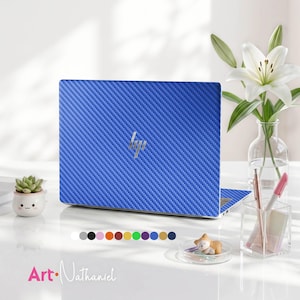 May include: A laptop with a blue carbon fiber textured skin featuring a silver HP logo in the center. The laptop is displayed alongside a small white succulent planter, a clear glass vase with a white lily, and a clear pen holder with pens.