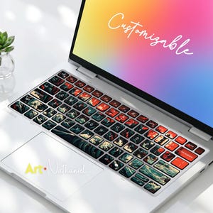 May include: A silver laptop featuring a keyboard skin with a dark wave and red sun graphic pattern. The screen displays a gradient background with the word Customizable in white script. The trackpad features the text Art Nathaniel in yellow and white.