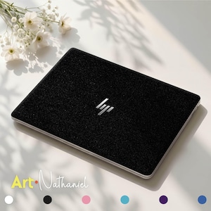 Op de afbeelding: Een zwarte laptopsticker met een getextureerde, glinsterende afwerking op de gesloten laptopdeksel. Het zilveren HP-logo is in het midden zichtbaar. De tekst Art Nathaniel verschijnt linksonder, gevolgd door zes gekleurde cirkels.