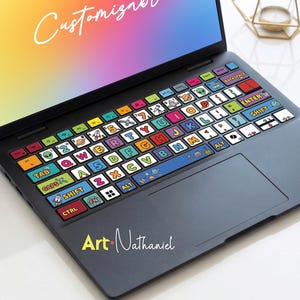 Peut inclure: Un clavier d'ordinateur portable avec des autocollants de touches personnalisés et colorés. Les autocollants présentent diverses illustrations, lettres et chiffres. Le texte "Customizer" est sur l'écran, et la signature de l'artiste "Art Nathaniel" est sur la surface de l'ordinateur portable.
