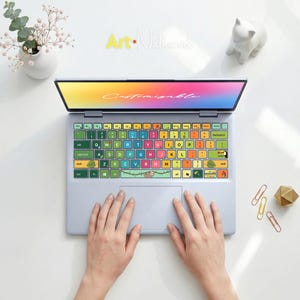 Peut inclure: Un ordinateur portable avec un clavier coloré orné d'un paresseux et de feuilles tropicales. L'écran affiche le mot "Customizable" dans un dégradé arc-en-ciel. L'ordinateur portable est ouvert, avec des mains posées sur le pavé tactile. Le fond comprend une figurine de chat blanc et un arrangement floral.