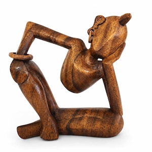 Op de afbeelding: Houten sculptuur van een liggende figuur, met het hoofd op een hand. De figuur is gesneden uit lichtbruin hout, met zichtbare nerfpatronen. Een ring zit om de arm van de figuur. De sculptuur heeft een gladde, gepolijste afwerking.