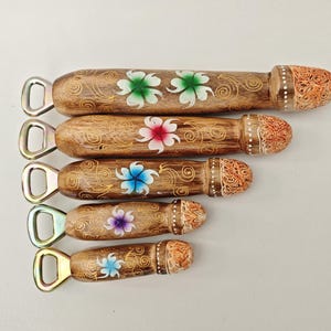 Peut inclure: Cinq ouvre-bouteilles en bois avec un design phallique. Les manches bruns présentent des motifs floraux peints en vert, rose, bleu et violet. Les extrémités sont sculptées et peintes avec des détails orange et blancs. L'ouvre-bouteille en métal est argenté.