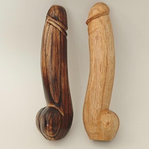 May include: Two wooden sculptures, one dark brown and one light brown, are displayed side by side. The sculptures are carved in a phallic shape, with detailed textures and rounded bases. The dark brown sculpture has a rich, polished finish, while the light brown one has a natural, unfinished look.