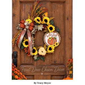 Peut inclure: Une couronne décorative avec des tournesols jaunes, du feuillage orange et marron, un ruban à motif léopard et un panneau circulaire blanc avec un dessin de citrouille et le texte hello fall. La couronne est fixée sur une porte en bois brun.