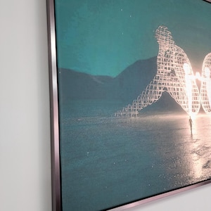 May include: A rectangular wall art piece featuring a teal-toned landscape with a large, glowing, wireframe sculpture of two figures sitting back-to-back. The artwork is encased in a thin, metallic frame with a dark, brushed finish.