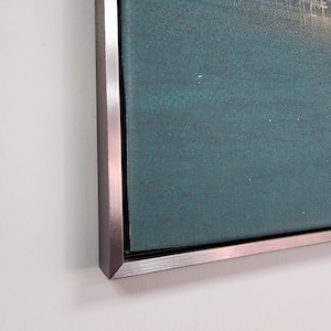 May include: A rectangular wall art piece featuring a deep teal canvas with a subtle textured surface. The artwork is encased in a metallic, brushed silver-toned frame with a clean, sharp edge, providing a modern and structured border.