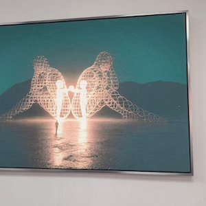 May include: A rectangular wall art piece in a silver frame featuring a teal landscape with two large, glowing, wireframe human figures sitting back-to-back. A small, dark silhouette of a person stands in the center, facing the bright light between the figures.