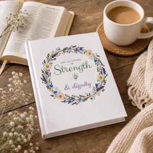 May include: A white journal with the text "She is clothed in Strength & dignity" surrounded by a floral wreath. An open book, a cup of coffee, and a knitted blanket are on a wooden surface.