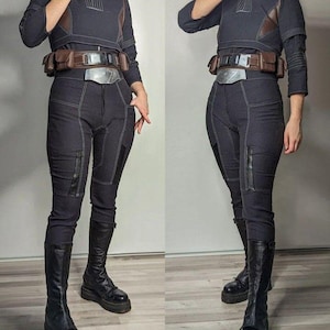 Puede incluir: Un disfraz de cosplay azul marino oscuro con una parte superior de cuello alto con detalles marrones, pantalones a juego y un cintur&oacute;n utilitario. El atuendo incluye botas negras hasta la rodilla. Costuras visibles.