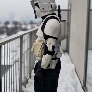 May include: A side view of a Star Wars Scout Trooper costume. The costume is mainly white and black, featuring a helmet, chest armour, and leg coverings. The trooper is standing outdoors in a snowy setting.