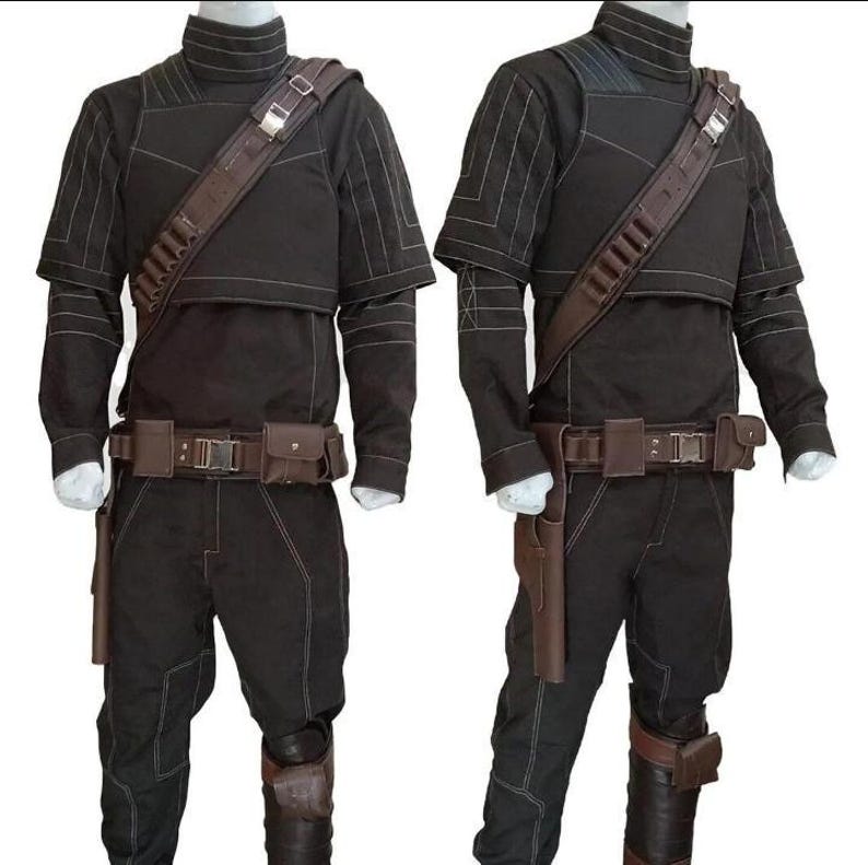May include: Two black costumes with brown detailing. Each outfit features a high-necked top, trousers, a belt with pouches, and a shoulder strap. The costumes have white stitching and brown holsters. The outfits are displayed on white mannequins.