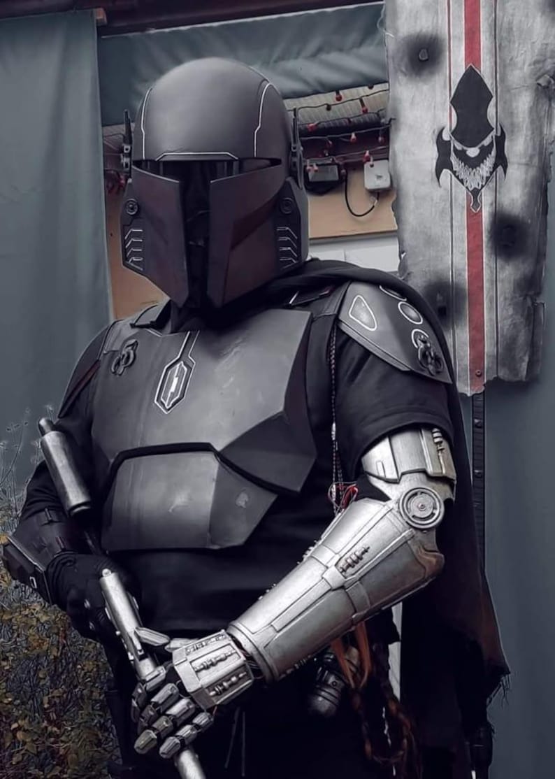 May include: A detailed costume of a Mandalorian warrior. The helmet, chest armor, and arm gauntlets are metallic gray. The costume includes a black cape and a blaster pistol. The overall design is reminiscent of a science fiction theme.