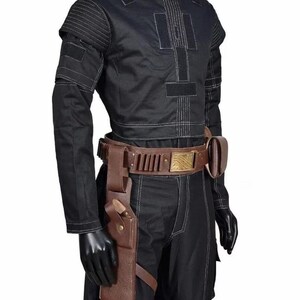 May include: Black costume with white stitching details, featuring a round-neck top and matching pants. A brown leather belt with a gold buckle and a holster with a strap are also included. The costume is displayed on a mannequin.