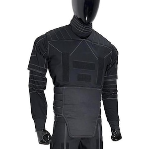 Pu&ograve; includere: Un completo tattico nero composto da maglia a maniche lunghe e pantaloni, con collo alto, pannelli imbottiti sul petto e in vita e cuciture bianche a contrasto. Il capo presenta inserti rettangolari in velcro sul petto e sulle gambe.