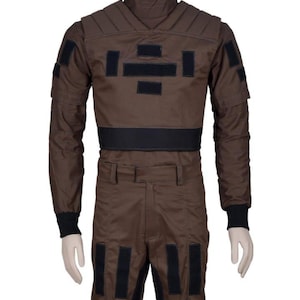 May include: Brown jumpsuit with black accents, featuring a high collar and multiple rectangular patches. The long-sleeved top has padded shoulders and a black belt. The pants have black patches near the knees and a straight leg design. The cuffs are black.