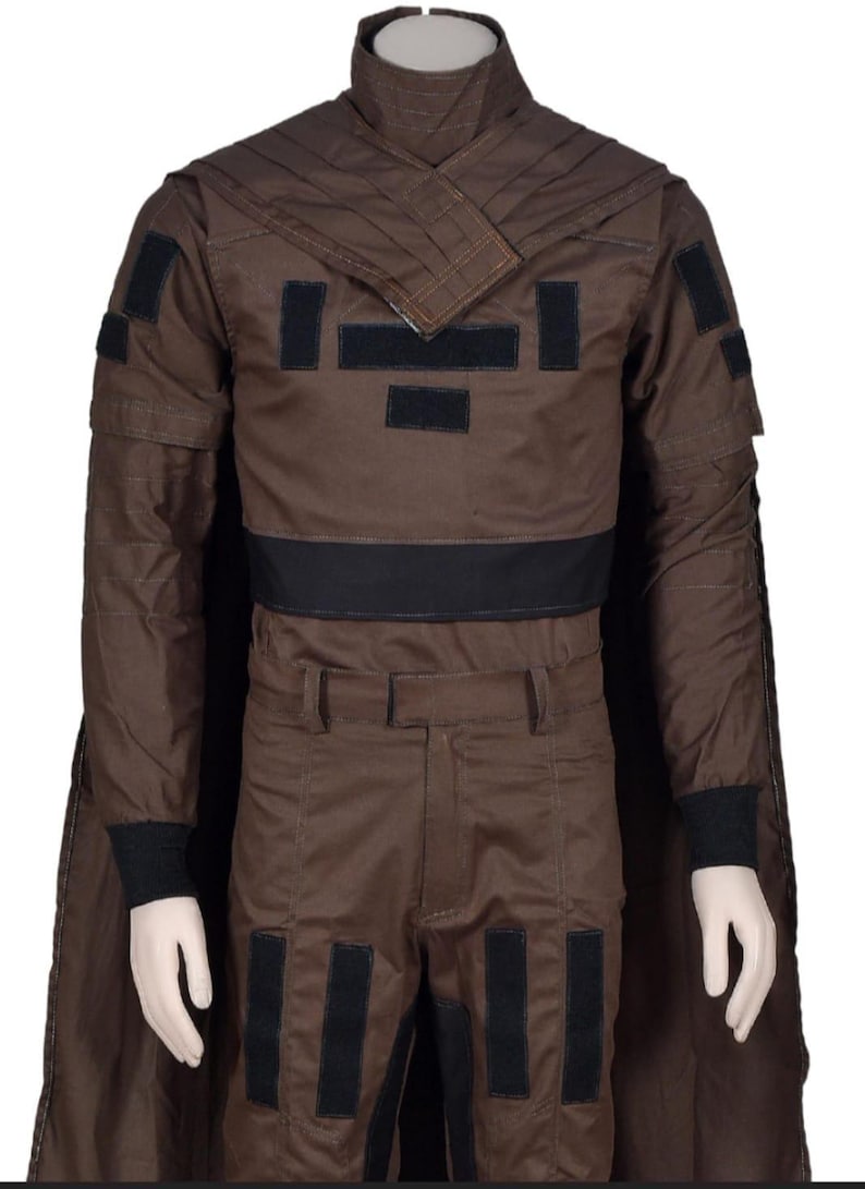 May include: Brown costume with a high collar, cape, and black accents. The outfit includes a jacket with black patches, matching pants, and black cuffs. The costume is displayed on a mannequin.