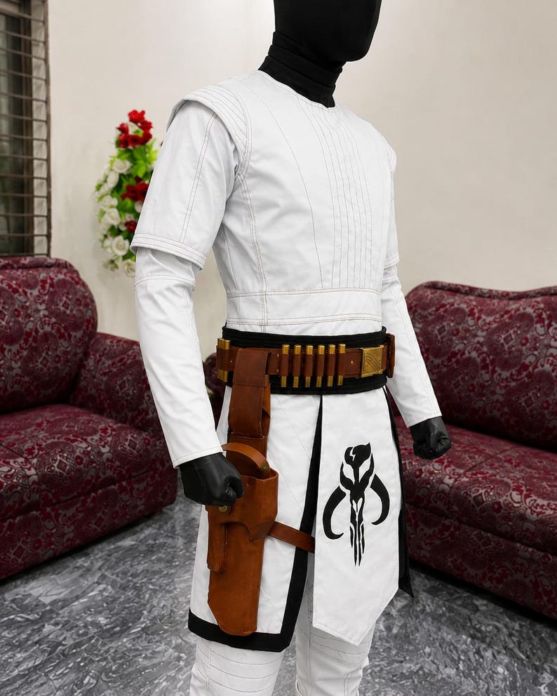 Puede incluir: Traje blanco con cintur&oacute;n negro y dorado, funda marr&oacute;n y un gr&aacute;fico negro en la parte delantera. El disfraz tiene mangas largas y cuello alto. El atuendo se exhibe en un maniqu&iacute;.