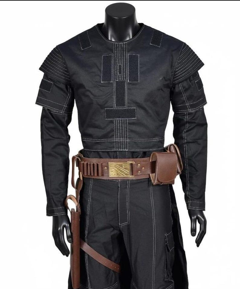 May include: Black costume with white stitching, displayed on a mannequin. The outfit includes a long-sleeved top with shoulder accents, matching pants, and a brown belt with a gold buckle. A holster and pouch are attached to the belt.