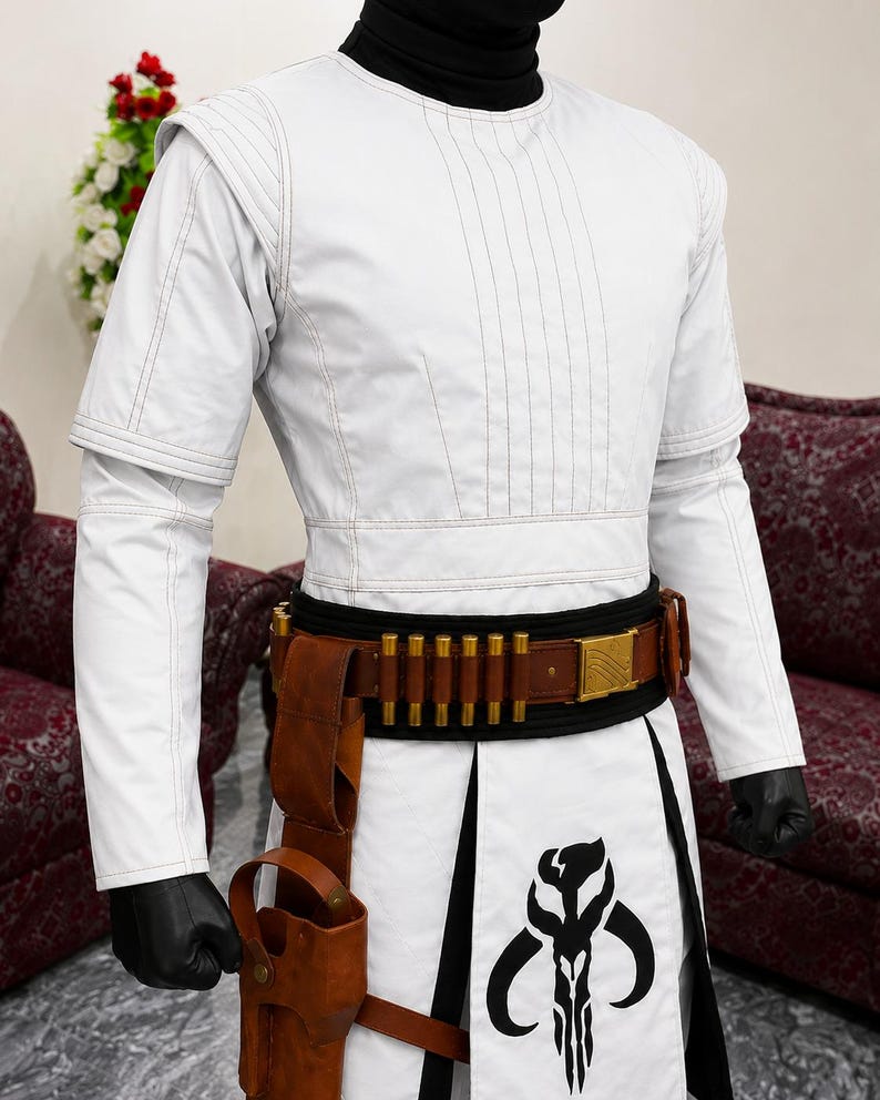 Puede incluir: Traje blanco con cuello alto negro, con un dise&ntilde;o detallado. El atuendo incluye un cintur&oacute;n marr&oacute;n con detalles dorados, una funda y una falda con un gr&aacute;fico en blanco y negro. Las mangas son largas y los guantes son negros.