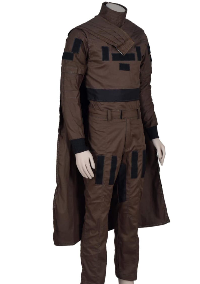 May include: Brown costume with black accents, including a long-sleeved top, pants, and a cape. The top features a high collar and black patches. The pants have black patches on the knees. The costume is displayed on a mannequin.