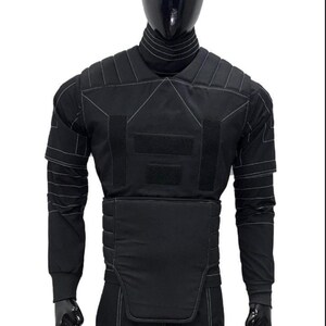 May include: Black tactical vest with white stitching details, displayed on a mannequin. The vest features multiple panels, including shoulder, chest, and waist protection. Long sleeves and a high collar are also visible.