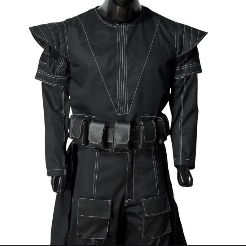 May include: Black costume with white stitching details. The outfit features a high collar, structured shoulders, long sleeves, and a belt with pouches. The pants have large pockets. The costume is displayed on a mannequin.