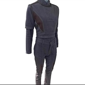 Puede incluir: Un conjunto de dos piezas gris oscuro con una parte superior de manga larga y pantalones. La parte superior tiene un cuello alto, mangas cortas y un cintur&oacute;n envolvente. Los pantalones tienen un dise&ntilde;o frontal &uacute;nico y parches en las rodillas. Costuras blancas acent&uacute;an el conjunto.