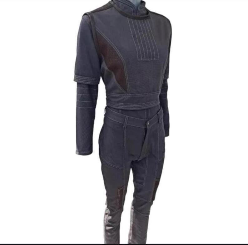 Puede incluir: Un conjunto de dos piezas gris oscuro con una parte superior de manga larga y pantalones. La parte superior tiene un cuello alto, mangas cortas y un cintur&oacute;n envolvente. Los pantalones tienen un dise&ntilde;o frontal &uacute;nico y parches en las rodillas. Costuras blancas acent&uacute;an el conjunto.