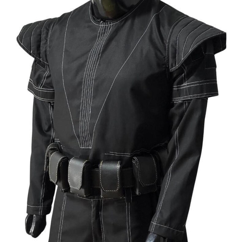 May include: Black costume with white stitching details. The outfit features structured shoulder pads, long sleeves, and a belt with multiple pouches. The design includes vertical and diagonal stitch lines, creating a unique visual texture. The costume appears to be made of a durable fabric.