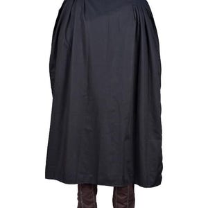 Puede incluir: Una capa negra con cuello alto y dise&ntilde;o fluido. La capa est&aacute; hecha de una tela oscura y se combina con botas marrones. La prenda parece ser un disfraz o ropa hist&oacute;rica.