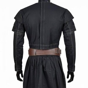 May include: Black jacket with white stitching details, featuring layered shoulder accents and long sleeves. A brown belt with rectangular accents cinches the waist. The jacket is paired with a black skirt, creating a cohesive outfit.