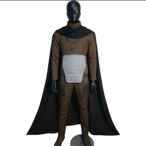 May include: A brown costume with a black cape, displayed on a mannequin. The outfit includes a high-collared jacket, pants, and a chest piece. The cape drapes over the shoulders, and the mannequin is on a round base.