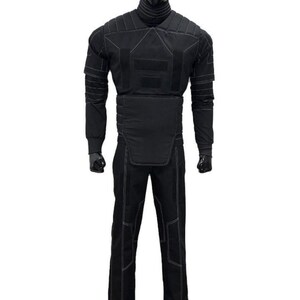 May include: A black protective suit displayed on a mannequin. The suit includes a long-sleeved top and pants, both with white stitching. The top features padded sections on the shoulders, chest, and arms. The pants have reinforced knee areas. The mannequin has a black head.