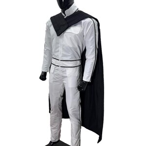 May include: A white jumpsuit with black trim and a black cape is displayed on a mannequin. The outfit includes a high collar, a black belt, and black gloves. The mannequin has a black head and is standing on a black base.