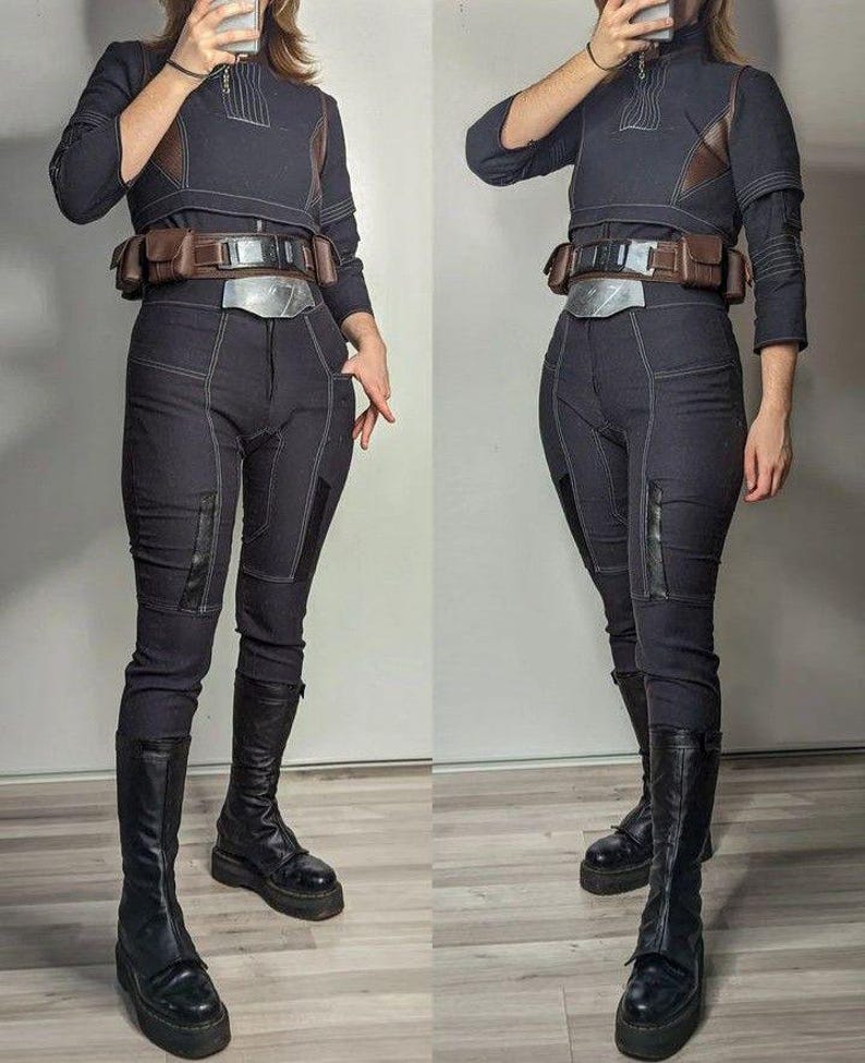 Puede incluir: Un disfraz de cosplay azul marino oscuro con una parte superior de cuello alto con detalles marrones, pantalones a juego y un cintur&oacute;n utilitario. El atuendo incluye botas negras hasta la rodilla. Costuras visibles.