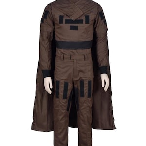 May include: A brown costume with a high collar, black accents, and a cape. The outfit includes a jacket, pants, and a belt. Black rectangular patches are on the jacket and pants. The costume is displayed on a mannequin.