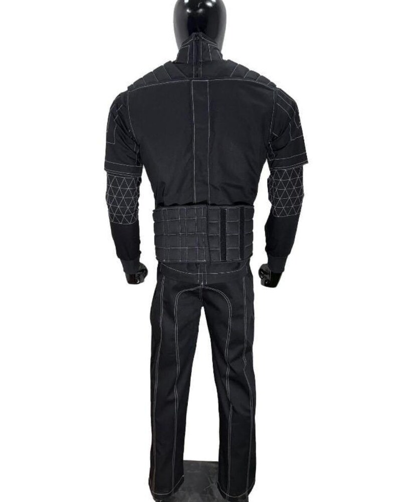 May include: Black tactical jumpsuit with white stitching details. The suit features a high collar, padded shoulders, and a segmented belt. The sleeves have a geometric pattern on the upper arms. The pants have a straight leg design.